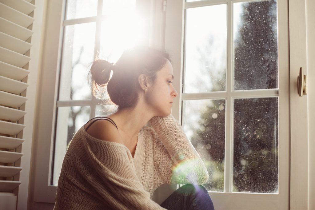 woman sitting next to window with depression